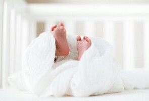Vauvan jalat näkyvät valkoisen peiton keskeltä pinnasängyssä.