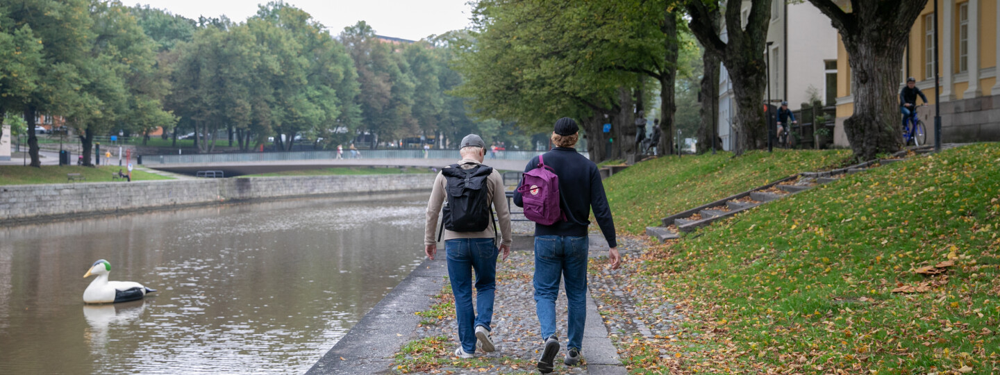 Kaksi opiskelijaa kävelee Aurajoen rannalla.