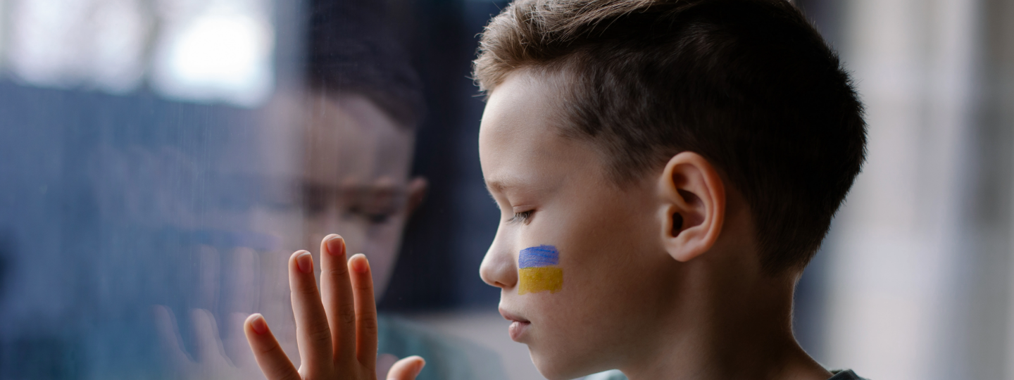 Lapsi ikkunalla, kasvoihin maalattu Ukrainan lippu.