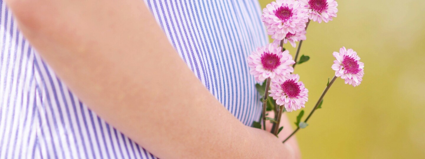 Raskaana oleva henkilö pitää kädessään kukkia, vain keskivartalo näkyy kuvassa.