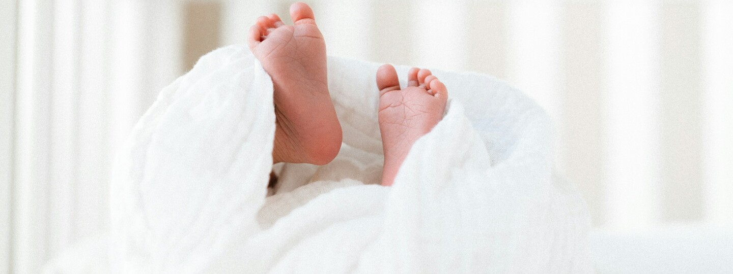 Vauvan jalat näkyvät valkoisen peiton keskeltä pinnasängyssä.