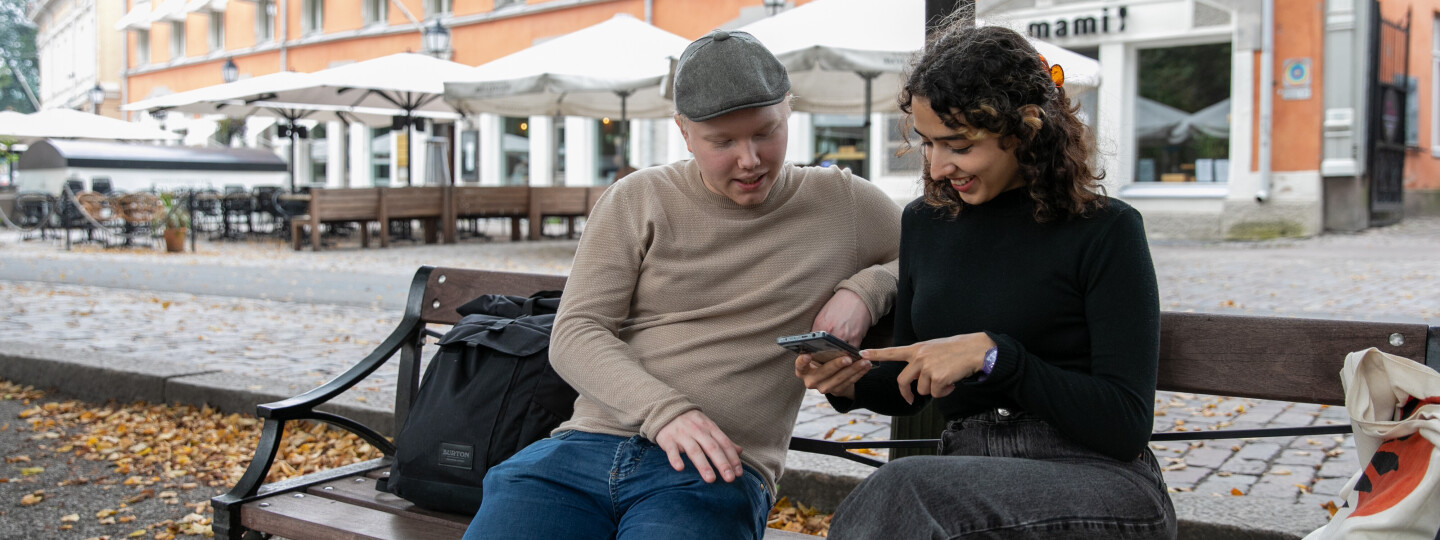 two students sitting on a bench looking at a mobile phone