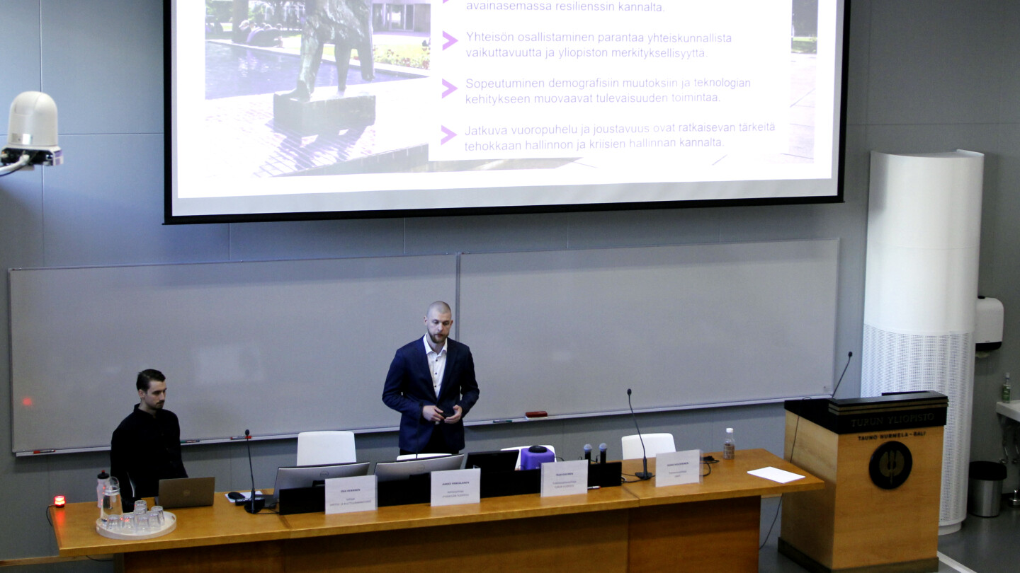 A man standing in front of a lecture room with a screen in the background