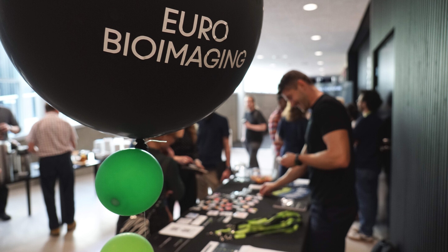 Ihmisiä esittelypöydän ääressä, etualalla Euro-BioImaging-ilmapallo