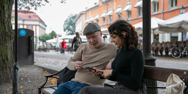 Two students sitting on a bench looking at a mobile phone