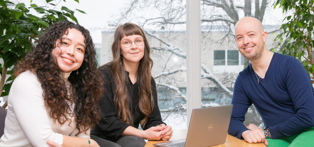 three doctoral researchers sitting at a table smiling and looking at the camera