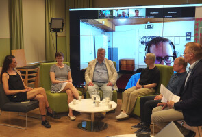 six people in a panel discussion with a screen showing remote participants in the background