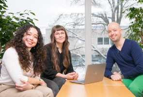 three doctoral researchers sitting at a table smiling and looking at the camera