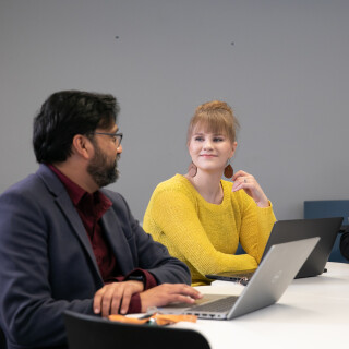 three people sitting together at a table with two laptops.