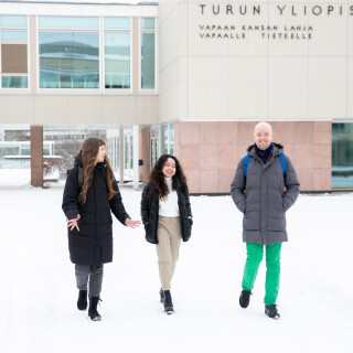 three people walking together in winter with university of turku main building in the background